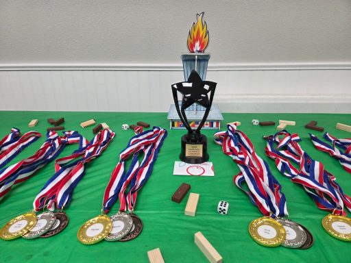 Board Game Olympics Awards Groups of three medals each surround a black trophy on a green tablecloth