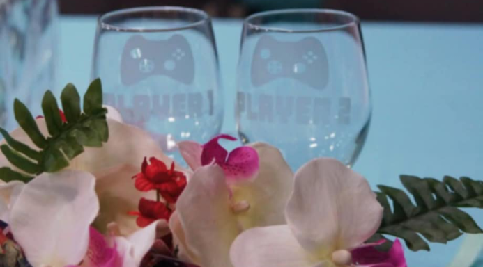 Fallout 4 Wedding Toasting Goblets Wineglasses etched with "Player 1" and "Player 2" on a blue tablecloth with orchids