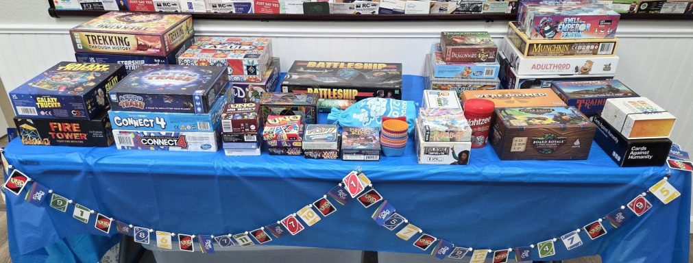 Board Game Olympics Table A table with a blue tablecloth covered with board games and decorated with an Uno card garland